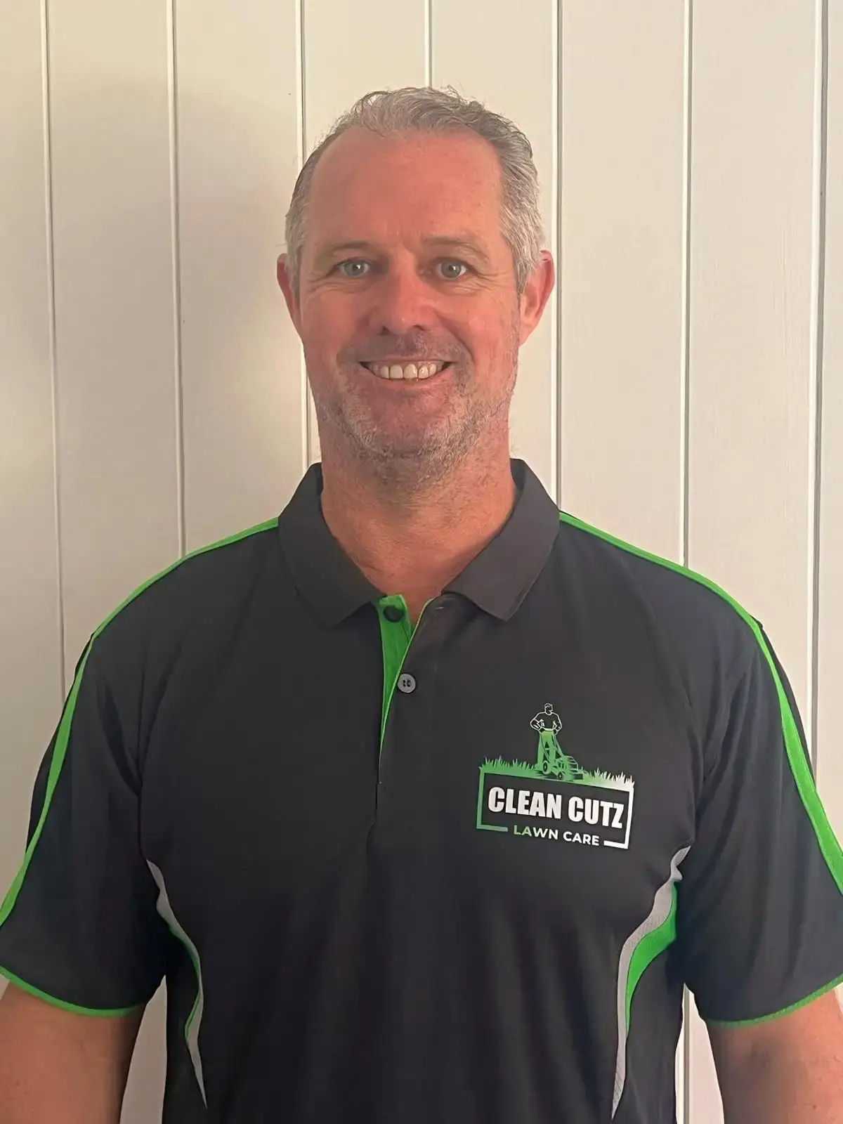 Owner of Clean Cutz Lawn Care smiling in a branded black and green polo shirt.
